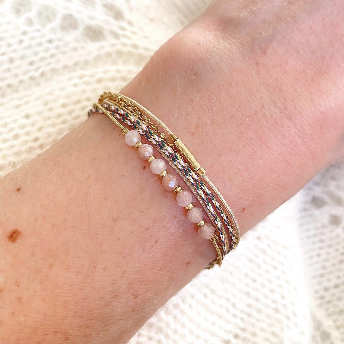 Bracelet composé de 4 liens en cordons dorés et chaîne dorée. Sur l'un d'eux sont montées 7 perles rondes de pierre naturelles de pierre de lune pêche.