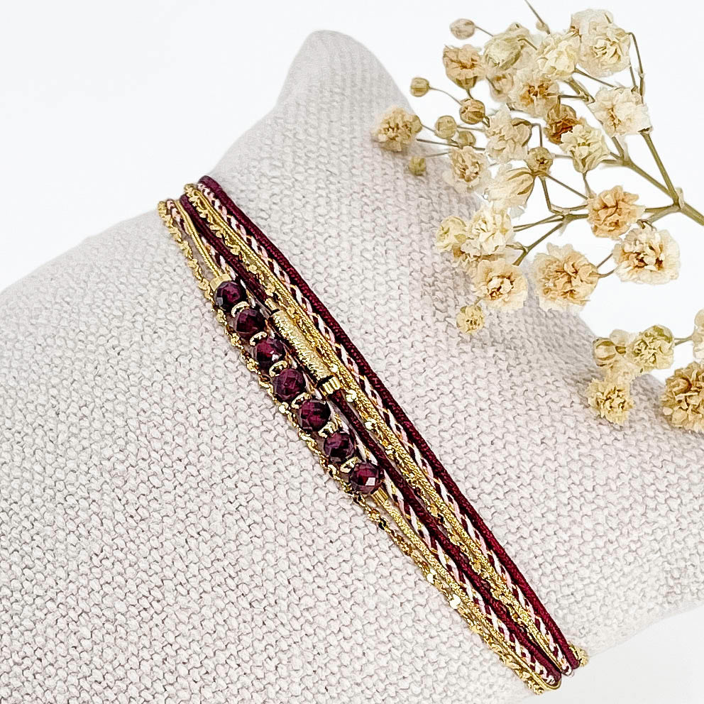 Bracelet composé de 4 liens en cordons doré et bordeaux et chaîne dorée. Sur l'un d'eux sont montées 7 perles rondes de pierre naturelles de Grenat.