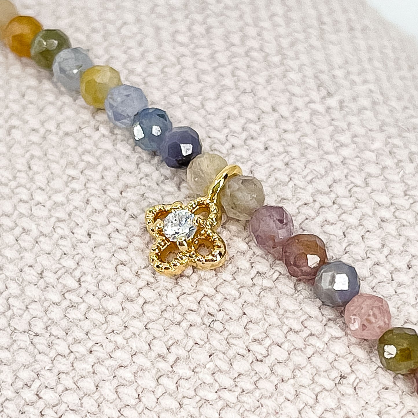 Bracelet pierres naturelles perles de tourmaline multicolores. En son centre un petit pendentif trèfle doré serti d'un cristal.