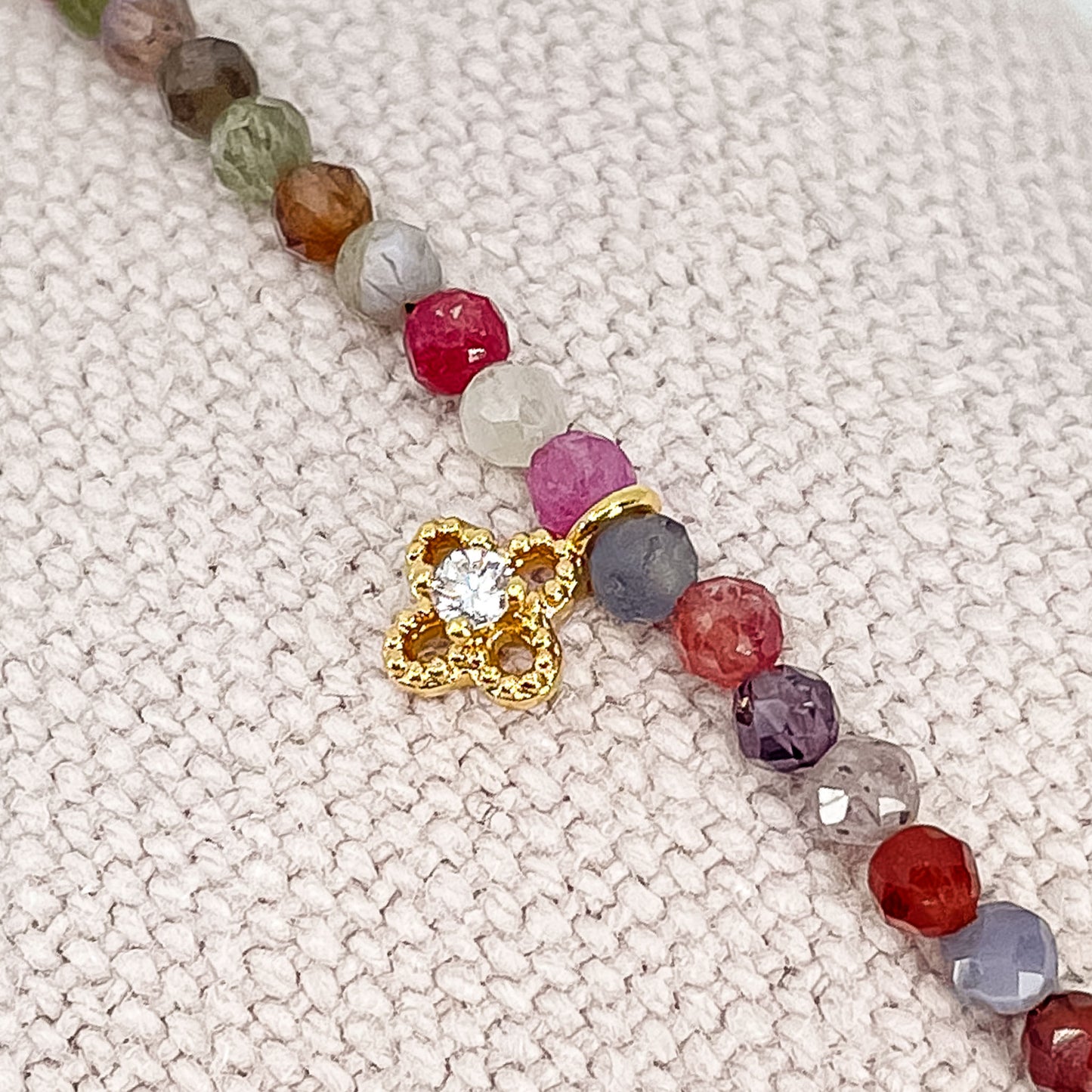 Bracelet pierres naturelles perles de tourmaline multicolores. En son centre un petit pendentif trèfle doré serti d'un cristal.