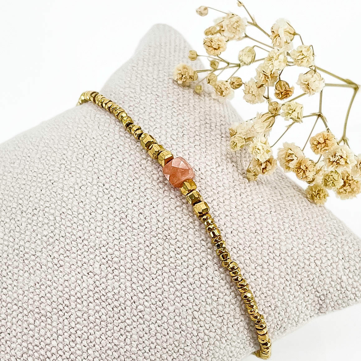 Bracelet mettant en lumière une perle cubique facettée de pierre fine naturelle de Jaspe rose pêche. Elle est entourée de perles d'hématites dorées.