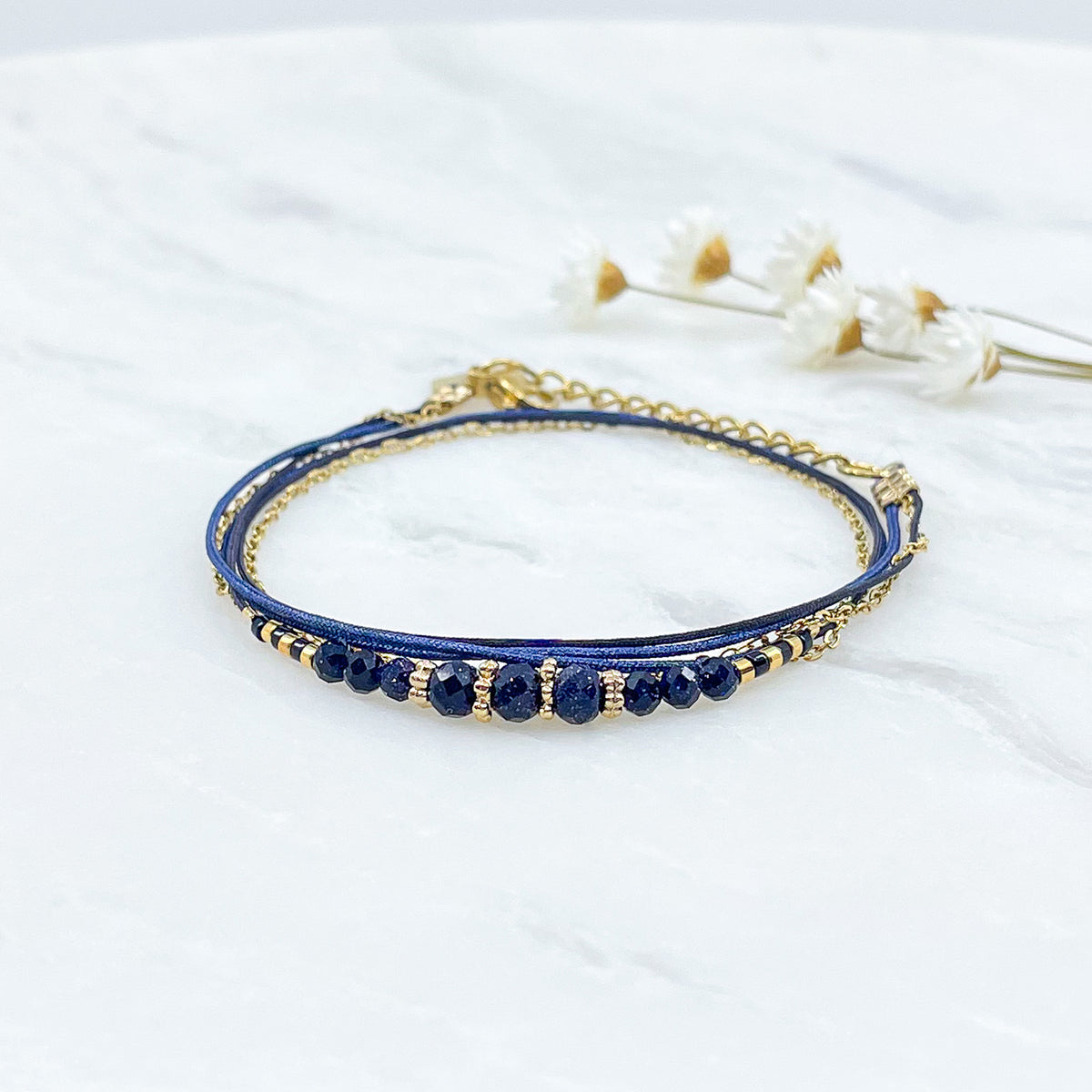 Bracelet en perles de cristal de verre bleu nuit. Trois liens de cordons et chaîne qui s'enroulent en deux tours sur le poignet. Jonc doré à l'or fin.