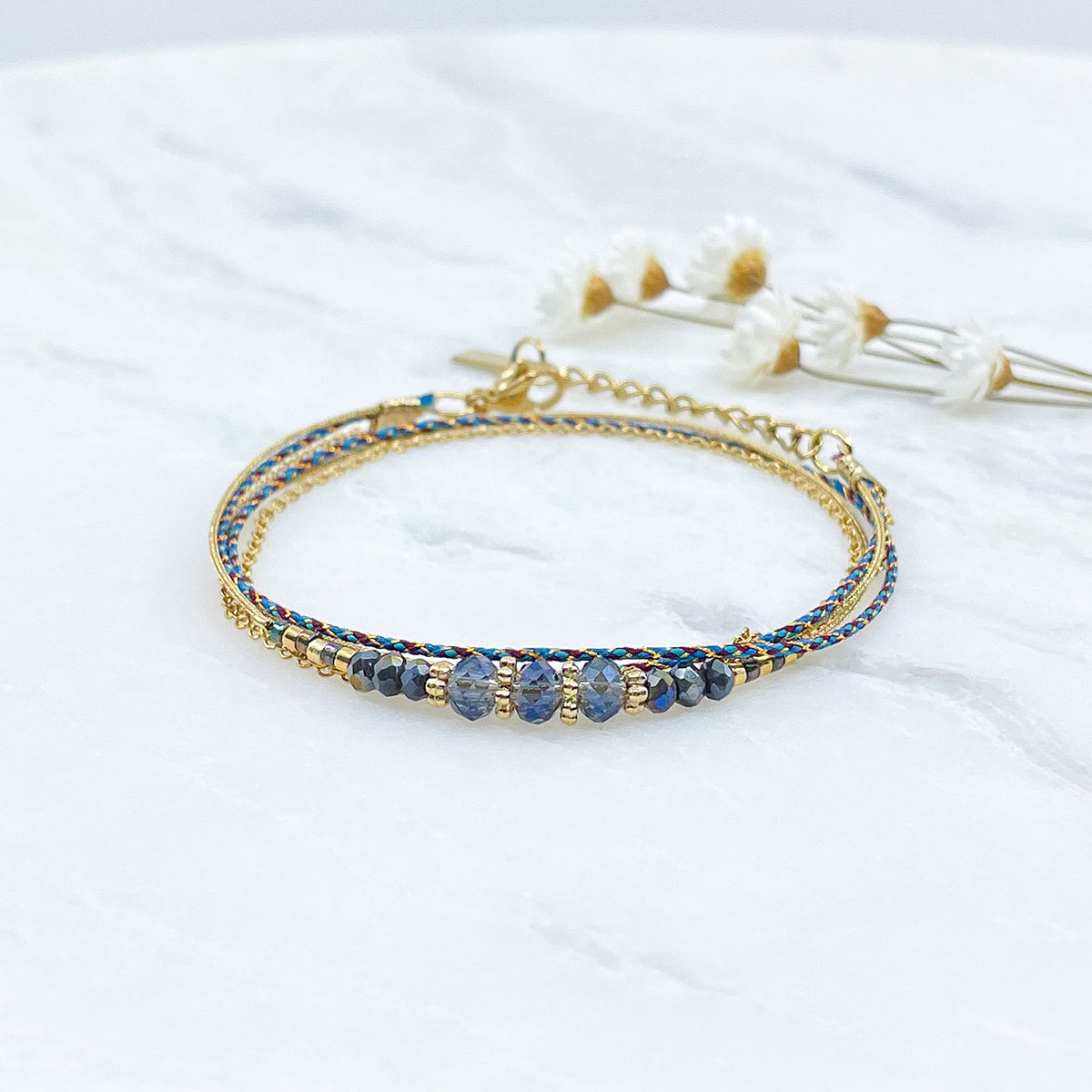 Bracelet composé de 3 liens en cordons colorés et doré et chaîne dorée. Sur l'un d'eux sont montées des perles de verre de Cristal bleu aux beaux reflets.