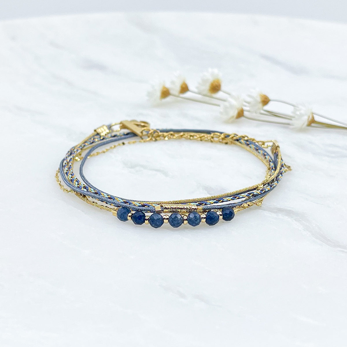 Bracelet composé de 4 liens en cordons doré et bleu et chaîne dorée. Sur l'un d'eux sont montées 7 perles rondes de pierre naturelles d'Agate bleue