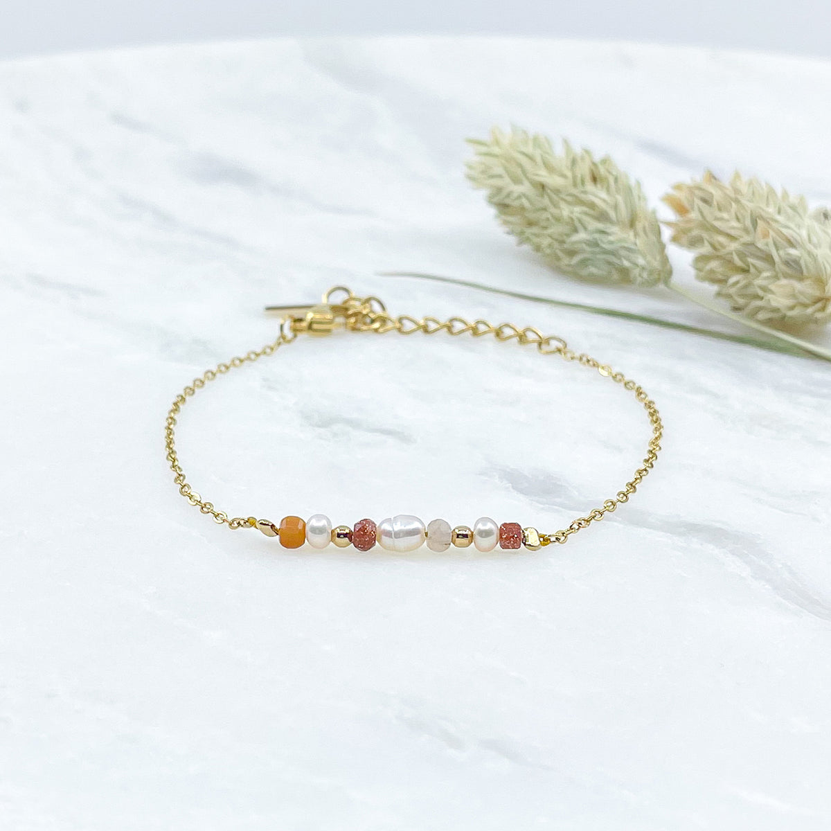 Bracelet monté avec une alternance de perles de culture et de pierres de lune naturelles et perle de verre pailletée de teinte terracotta sur une chaîne dorée.