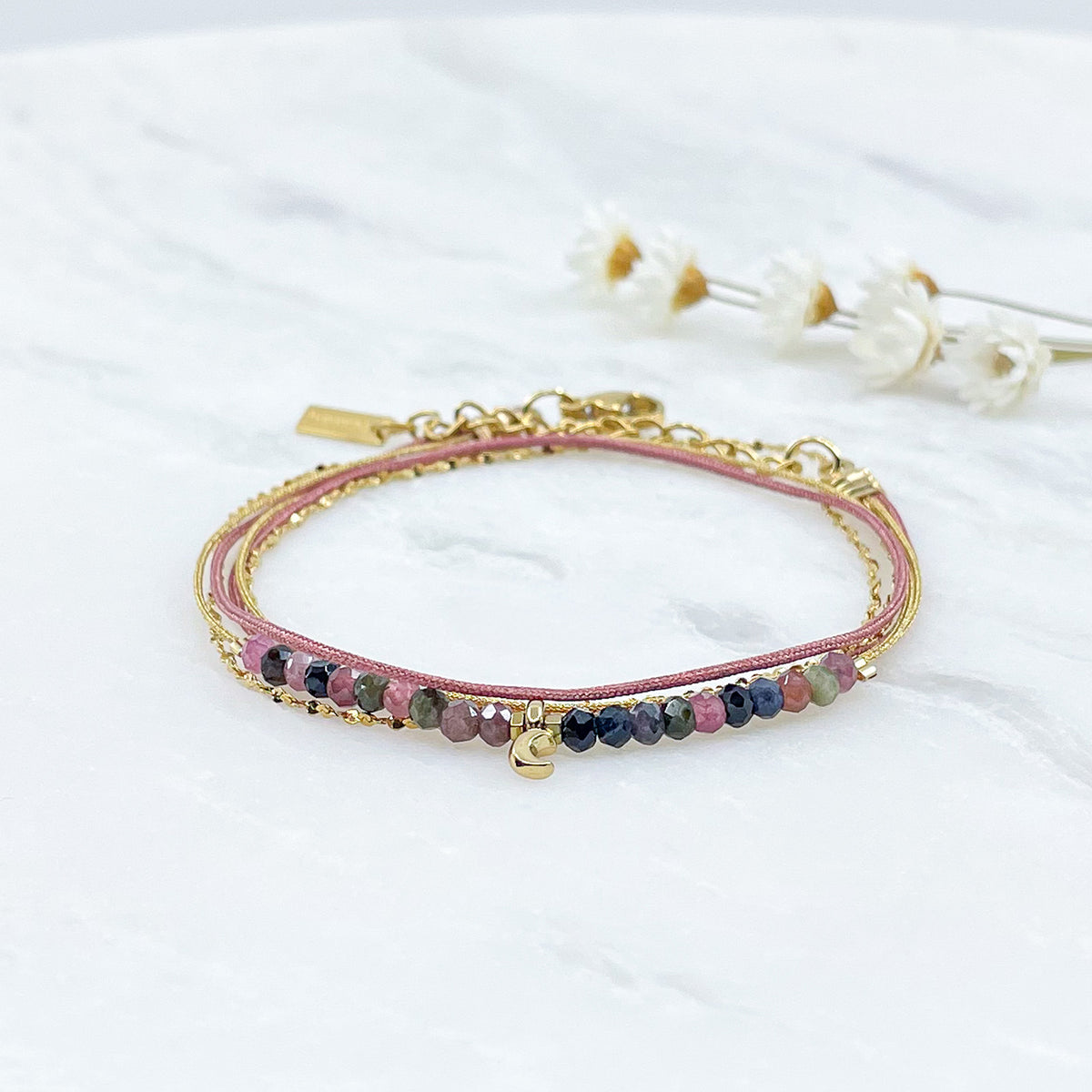 Bracelet composés de plusieurs liens cordons et chaine doré et rose s'enroulant autour du poignet. Sur un cordon des perles de pierre naturelle de tourmalines multicolores sont ponctuées par un pendentif croissant de lune doré.