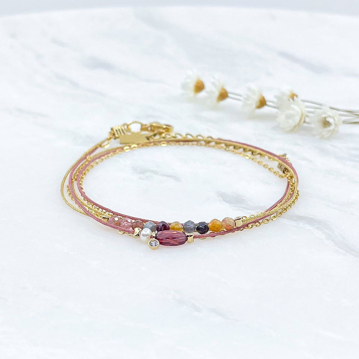 Bracelet composé de 3 liens cordons et chaîne s'enroulant en deux tours sur le poignet. Il met en valeur les perles de pierre naturelle de Tourmaline ainsi qu'un Grenat, une Perle de Culture et un petit pendentif serti d'un cristal. Pierres et perles sont montées sur les différents liens.