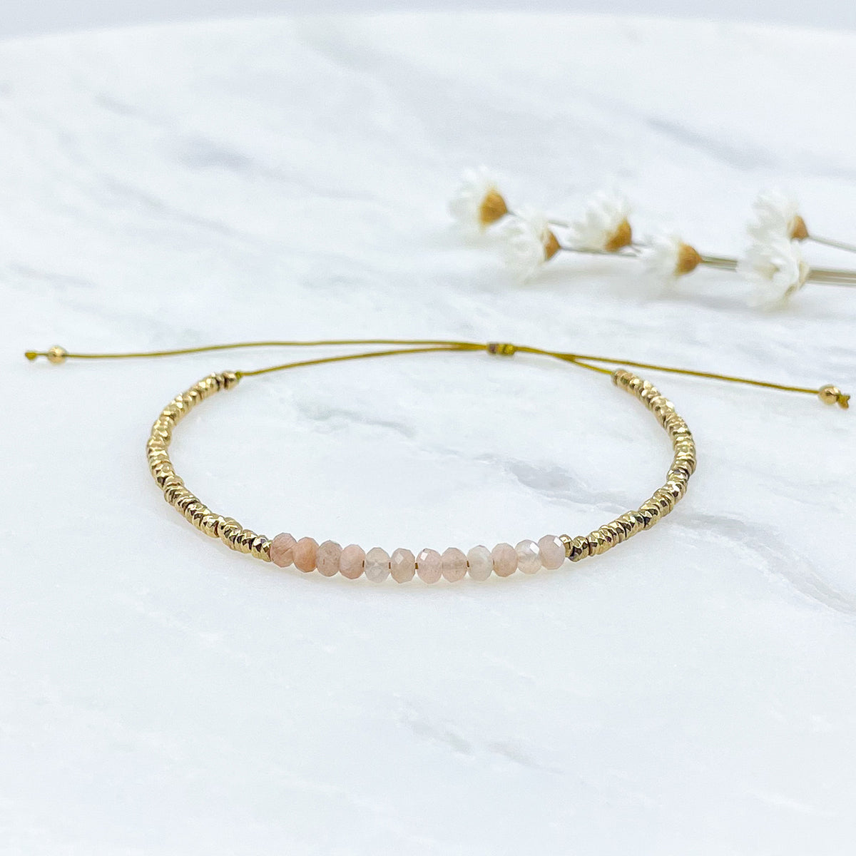 Bracelet ajustable en pierres fines naturelles Pierre de Soleil aux nuances rosées et perles d'hématites dorées.