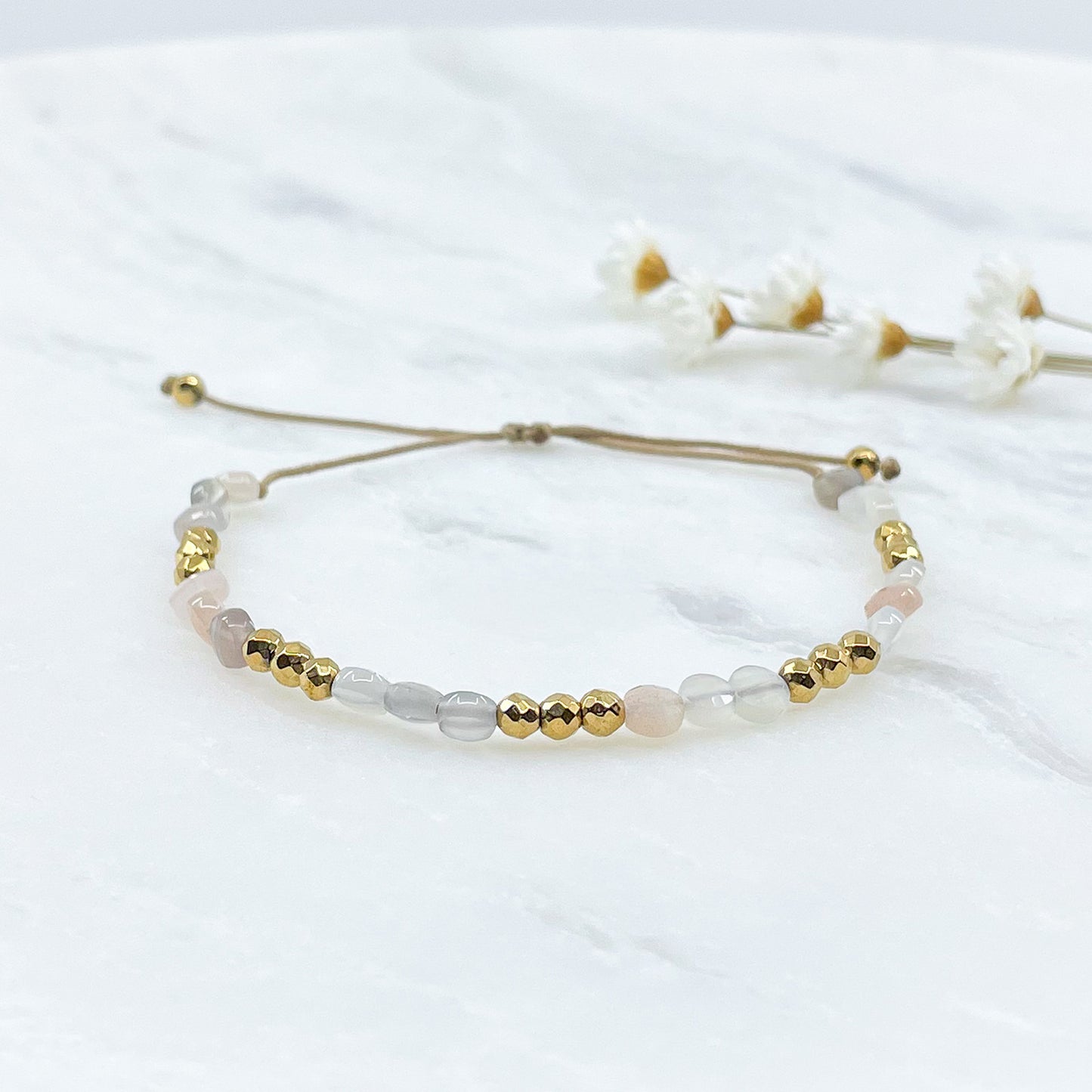 Bracelet ajustable en pierres fines naturelles Pierre de Soleil aux nuances blanches et rosées et perles d'hématites dorées.