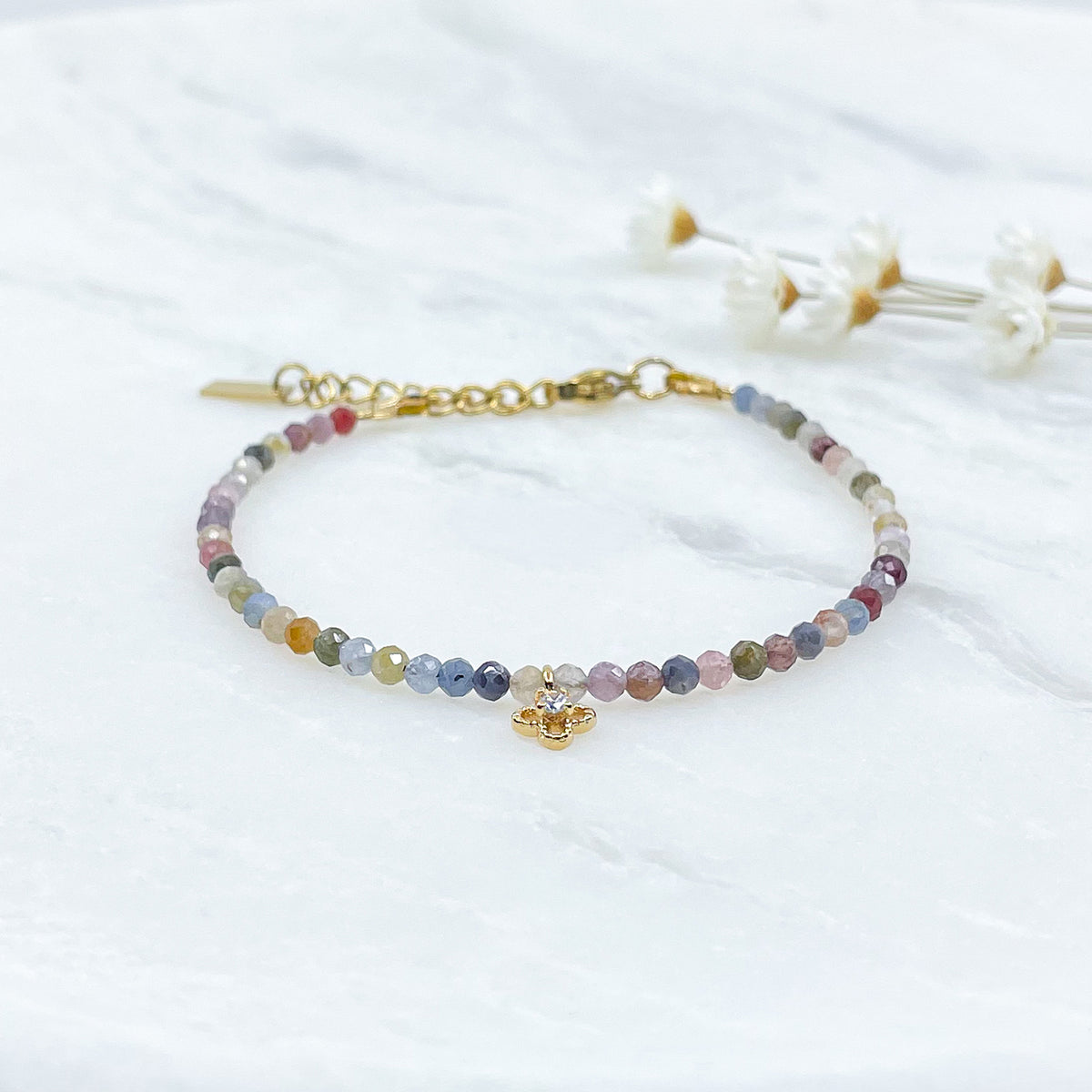 Bracelet pierres naturelles perles de tourmaline multicolores. En son centre un petit pendentif trèfle doré serti d'un cristal.