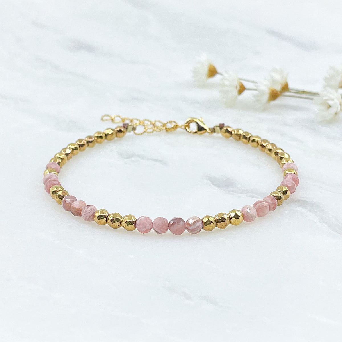 Rivière en pierres fines naturelles en perles facettées rose de rhodochrosite alternant avec des perles d'hématite dorée.