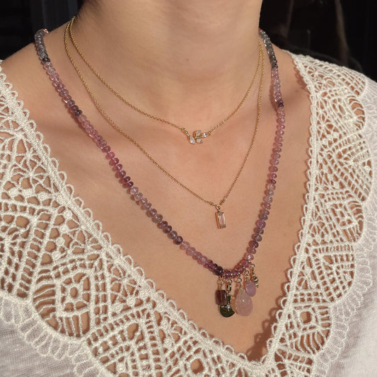 Collier long de 58 cm en pierres fines naturelles de spinelle dans des dégradés de rose à bleu gris. 5 charms : 3 pierres fines naturelles de teintes harmonieuses, une médaille ronde et un pendentif en petites perles plaqué or. Chaîne de réglage de 4 cm et fermoir plaqué or 18 carats