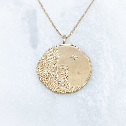 Long collier en chaîne maille forçat de 50 cm. Médaille de 2.6 cm de diamètre au contours irréguliers représentant de beaux feuillages et petit éclat scintillant en forme d'étoile. Or mat en partie recyclé couleur champagne