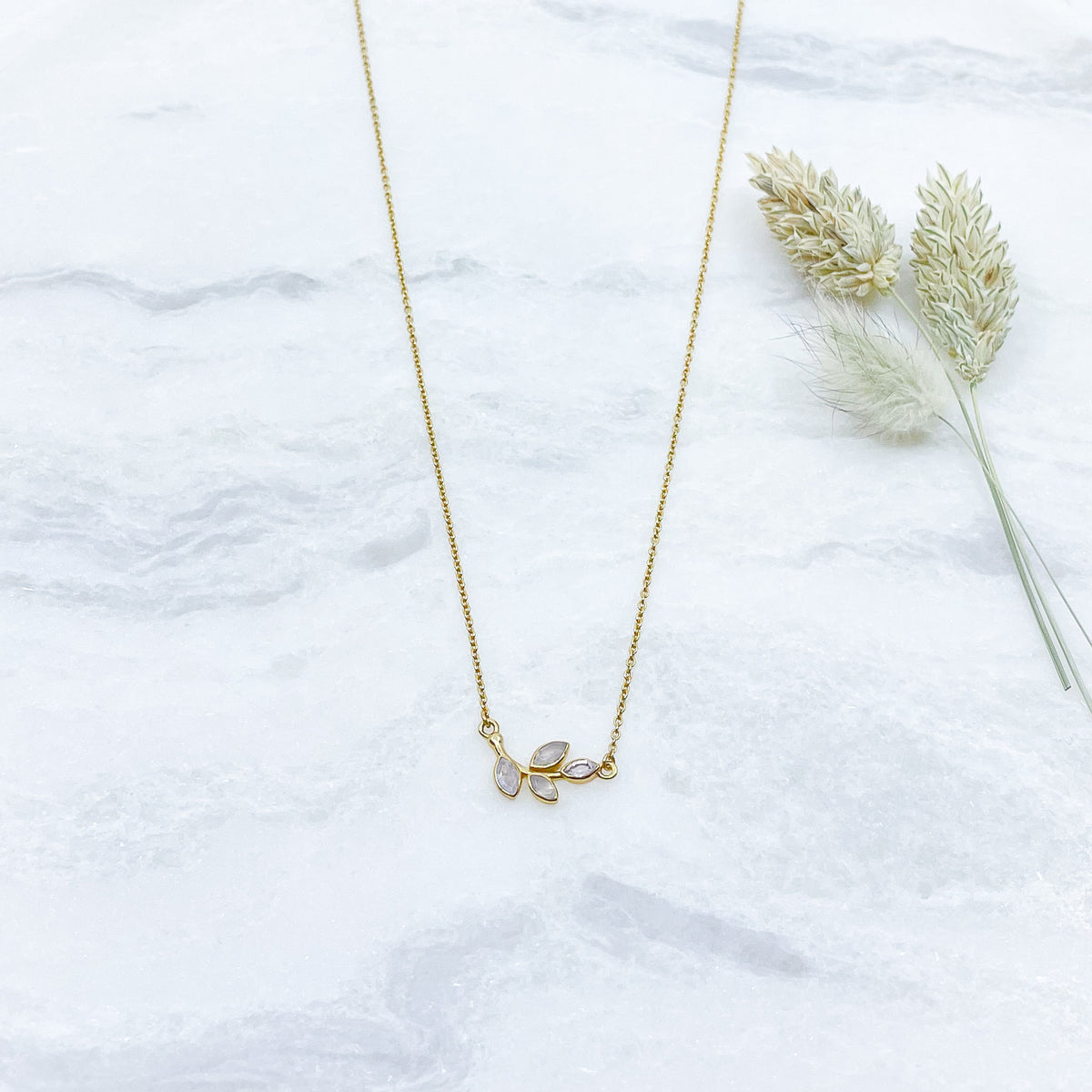 Collier plaqué or avec chaîne ajustable sur 3 niveaux de longueur différentes de 37 à 45 cm. Il met en valeur une brindille de feuillage réalisée en pierres fines naturelles de Pierre de Lune blanche au beaux reflets.