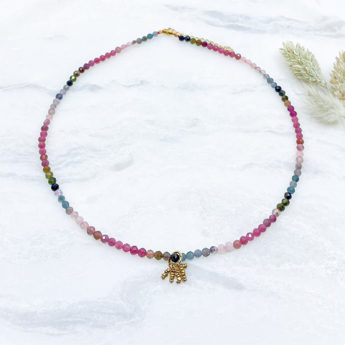 Collier rivière de perles de pierres fines naturelles de Tourmaline teinte arc-en-ciel. Pendentif composé de petites pierres d'hématite dorée. Chaîne de fermeture ajustable de 39 à 44 cm.