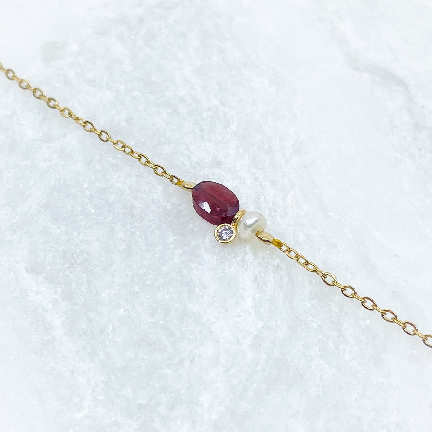 Collier en pierre fine naturelle Grenat orné d'une perle de culture et d'un petit pendentif cristal éclatant. Monté sur chaîne dorée en acier inoxydable.