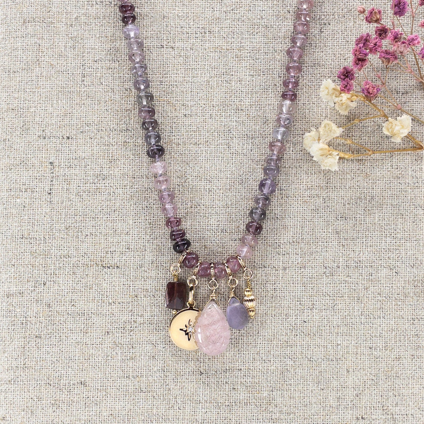 Collier long de 58 cm en pierres fines naturelles de spinelle dans des dégradés de rose à bleu gris. 5 charms : 3 pierres fines naturelles de teintes harmonieuses, une médaille ronde et un pendentif en petites perles plaqué or. Chaîne de réglage de 4 cm et fermoir plaqué or 18 carats