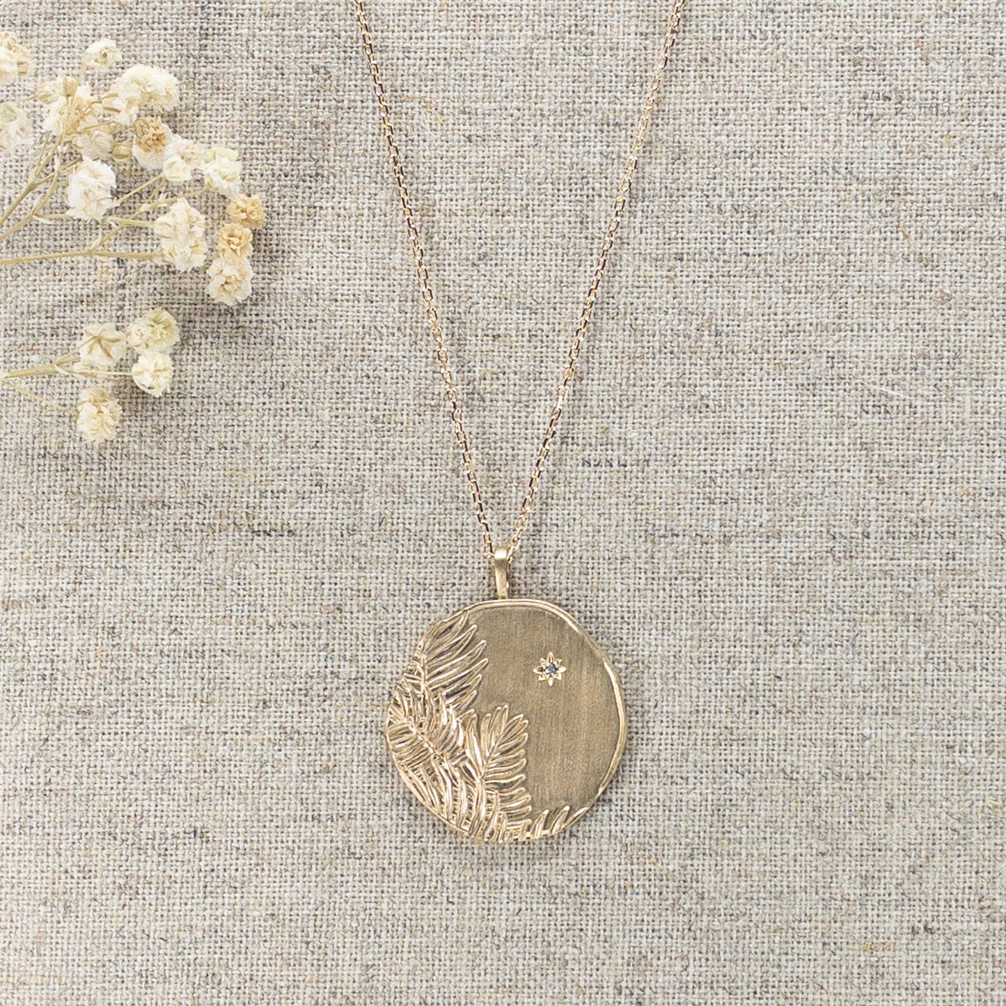 Long collier en chaîne maille forçat de 50 cm. Médaille de 2.6 cm de diamètre au contours irréguliers représentant de beaux feuillages et petit éclat scintillant en forme d'étoile. Or mat en partie recyclé couleur champagne