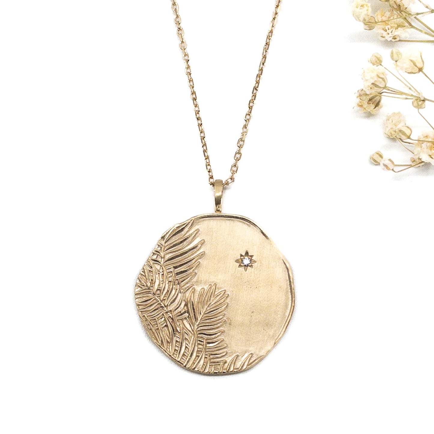 Long collier en chaîne maille forçat de 50 cm. Médaille de 2.6 cm de diamètre au contours irréguliers représentant de beaux feuillages et petit éclat scintillant en forme d'étoile. Or mat en partie recyclé couleur champagne
