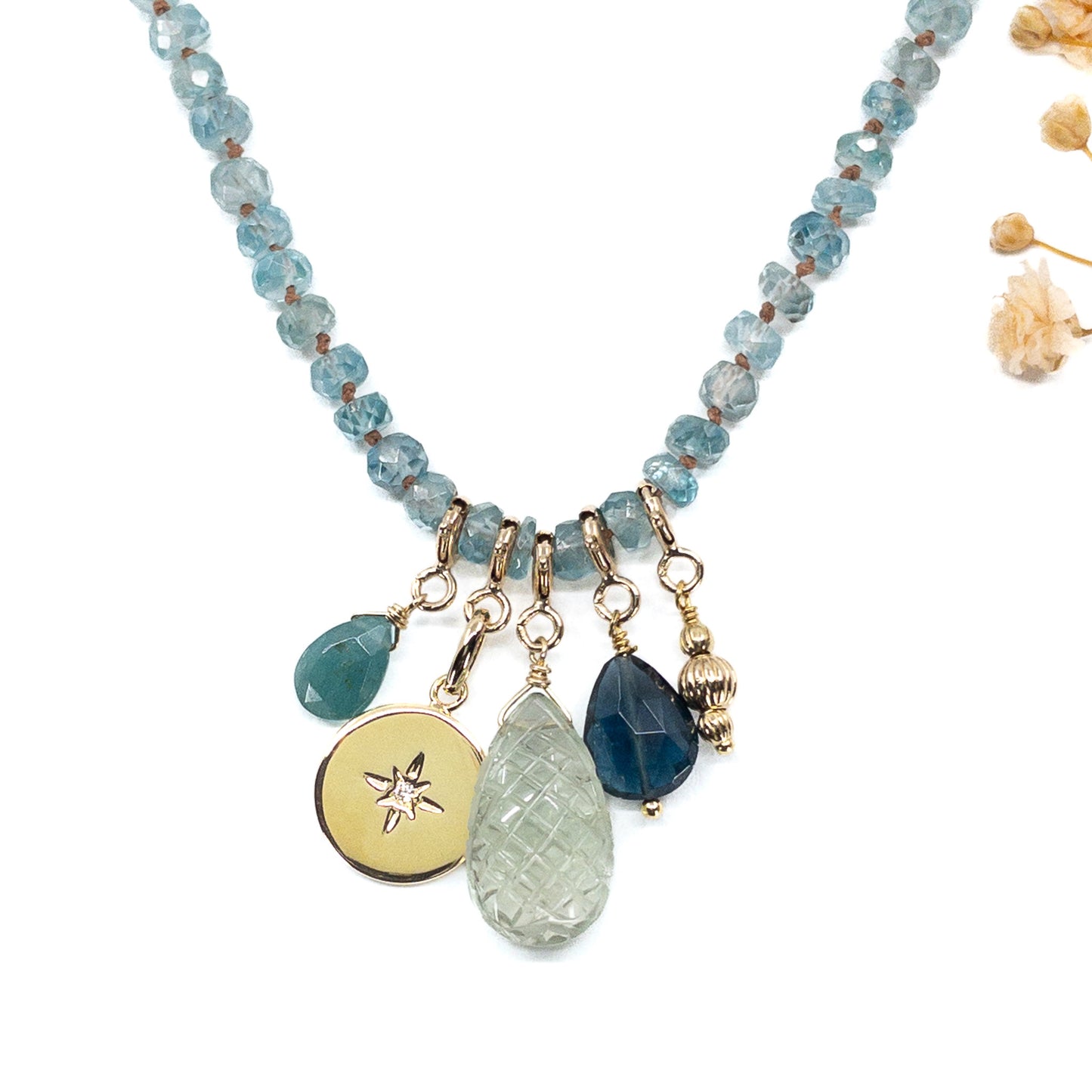 Collier long de 60 cm en pierres fines de zircon naturel d'un bleu azur. 5 charms : 3 pierres fines naturelles de teintes bleu-vert, une médaille ronde et un pendentif en petites perles plaqué or. Chaîne de réglage de 4 cm et fermoir plaqué or 18 carats