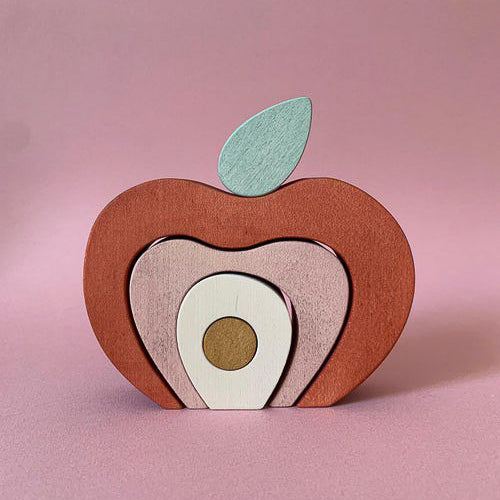 Jeu en bois en forme de pomme composé de différents éléments empilables. Teinte rouge rosée. A partir de 3 ans.