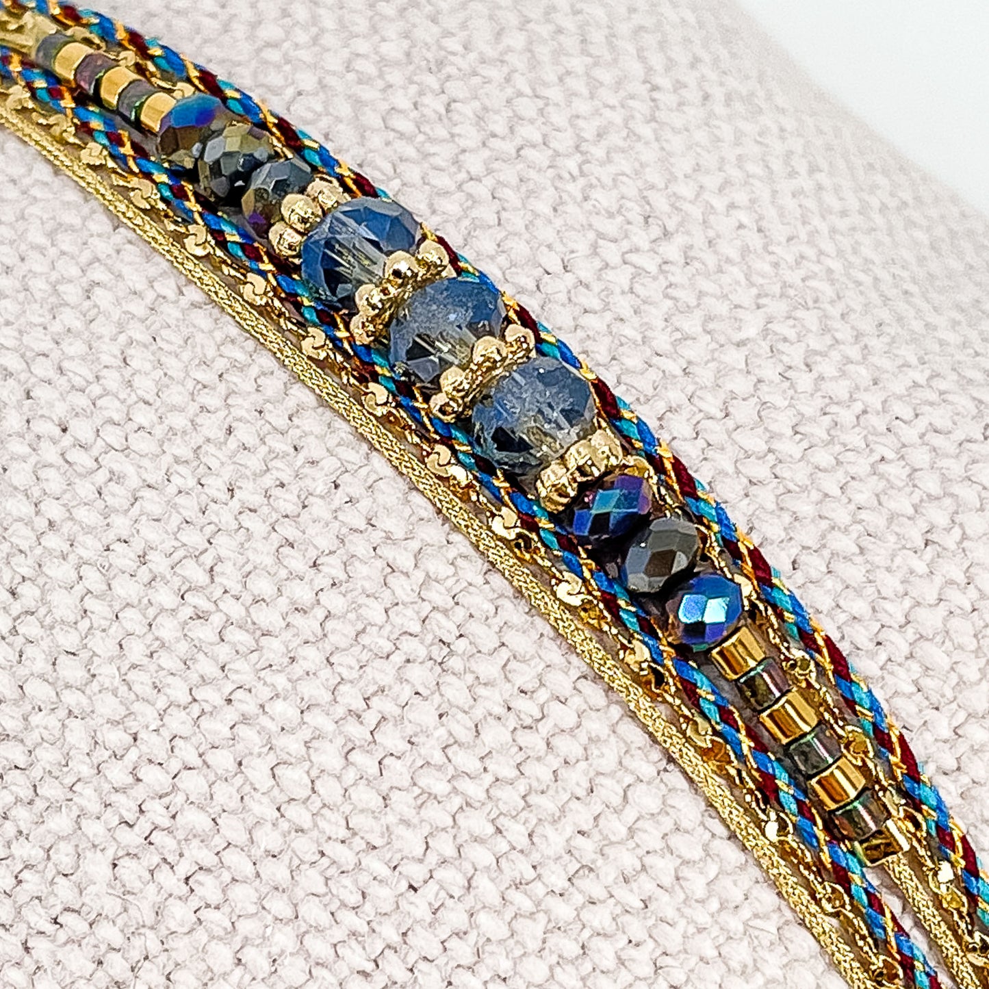 Bracelet composé de 3 liens en cordons colorés et doré et chaîne dorée. Sur l'un d'eux sont montées des perles de verre de Cristal bleu aux beaux reflets.