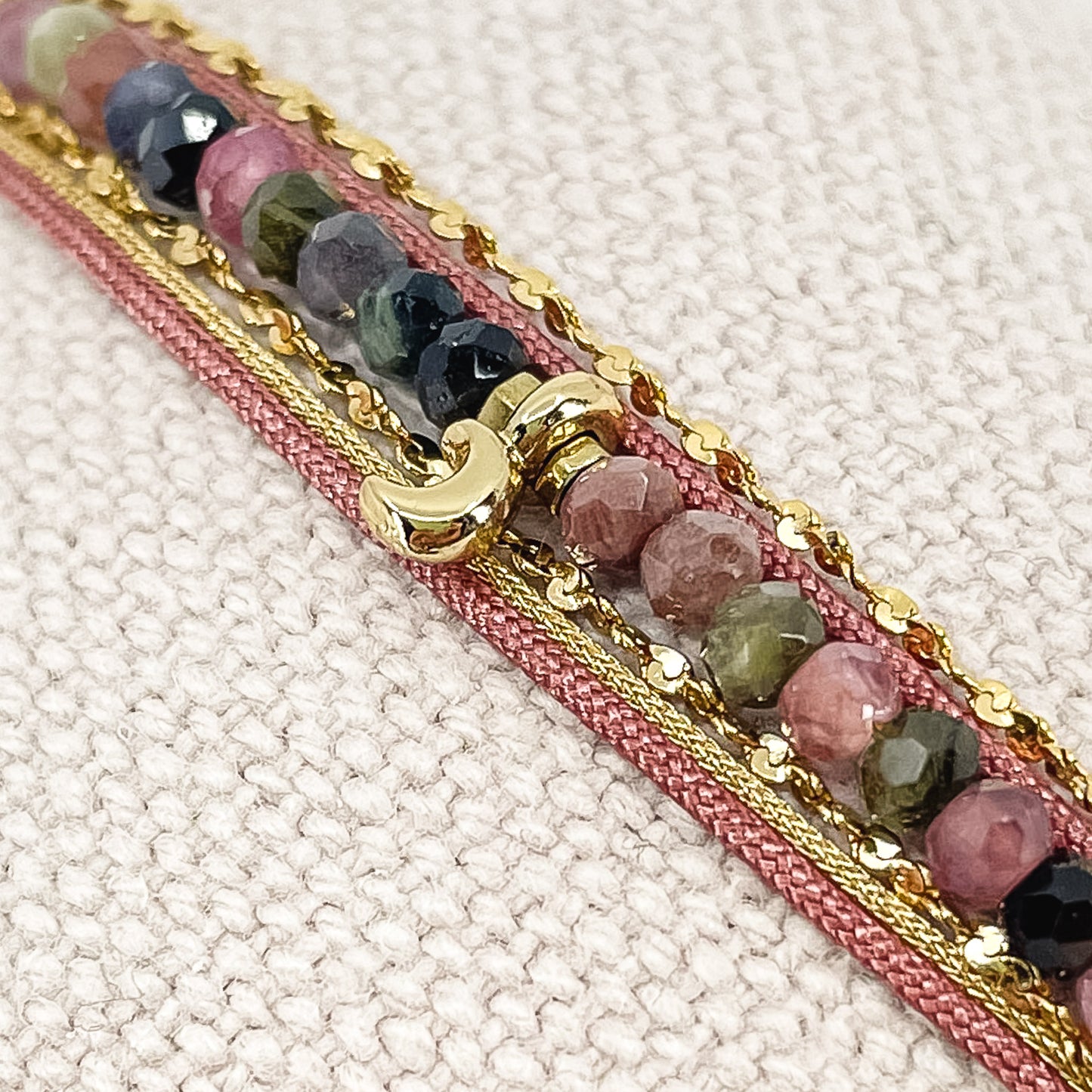Bracelet composés de plusieurs liens cordons et chaine doré et rose s'enroulant autour du poignet. Sur un cordon des perles de pierre naturelle de tourmalines multicolores sont ponctuées par un pendentif croissant de lune doré.
