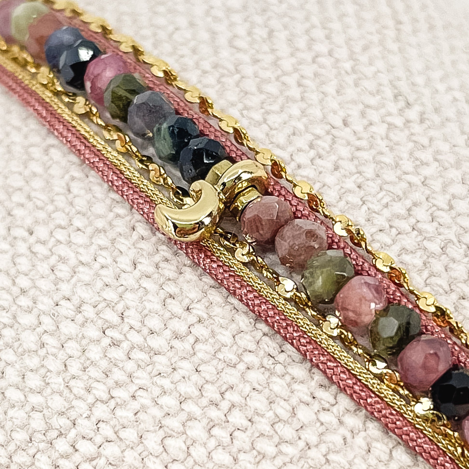 Bracelet composés de plusieurs liens cordons et chaine doré et rose s'enroulant autour du poignet. Sur un cordon des perles de pierre naturelle de tourmalines multicolores sont ponctuées par un pendentif croissant de lune doré.