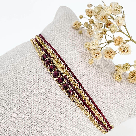 Bracelet composé de 4 liens en cordons doré et bordeaux et chaîne dorée. Sur l'un d'eux sont montées 7 perles rondes de pierre naturelles de Grenat.