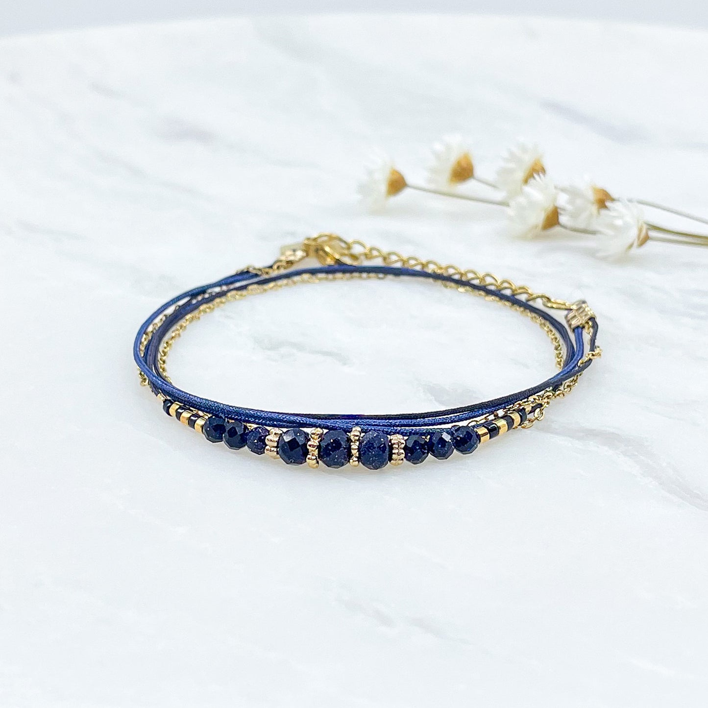 Bracelet en perles de cristal de verre bleu nuit. Trois liens de cordons et chaîne qui s'enroulent en deux tours sur le poignet. Jonc doré à l'or fin. 