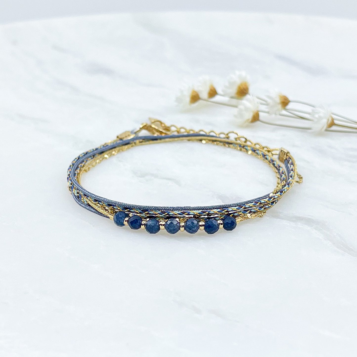 Bracelet composé de 4 liens en cordons doré et bleu et chaîne dorée. Sur l'un d'eux sont montées 7 perles rondes de pierre naturelles d'Agate bleue