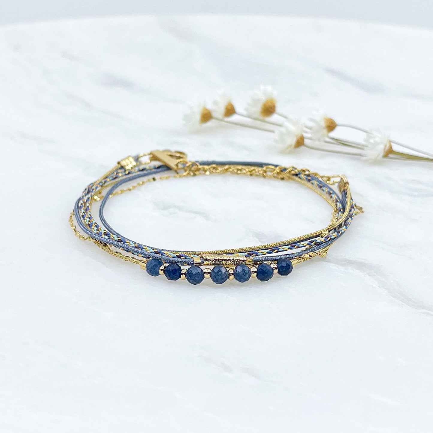 Bracelet composé de 4 liens en cordons doré et bleu et chaîne dorée. Sur l'un d'eux sont montées 7 perles rondes de pierre naturelles d'Agate bleue