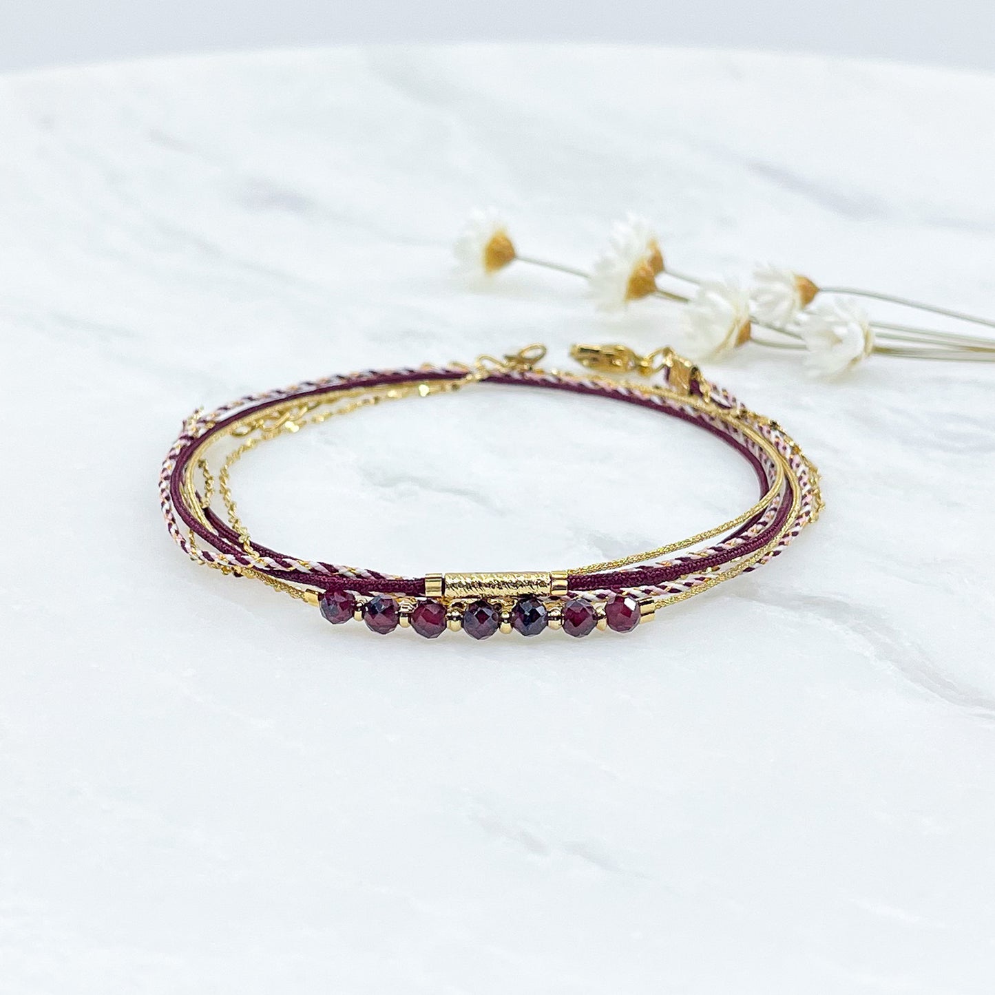 Bracelet composé de 4 liens en cordons doré et bordeaux et chaîne dorée. Sur l'un d'eux sont montées 7 perles rondes de pierre naturelles de Grenat.