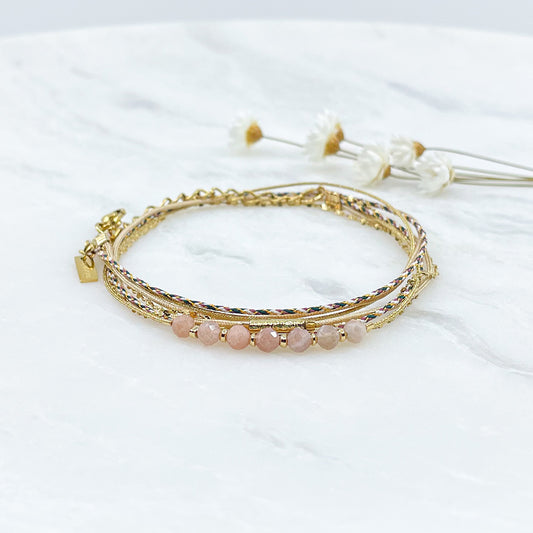 Bracelet composé de 4 liens en cordons dorés et chaîne dorée. Sur l'un d'eux sont montées 7 perles rondes de pierre naturelles de pierre de lune pêche.