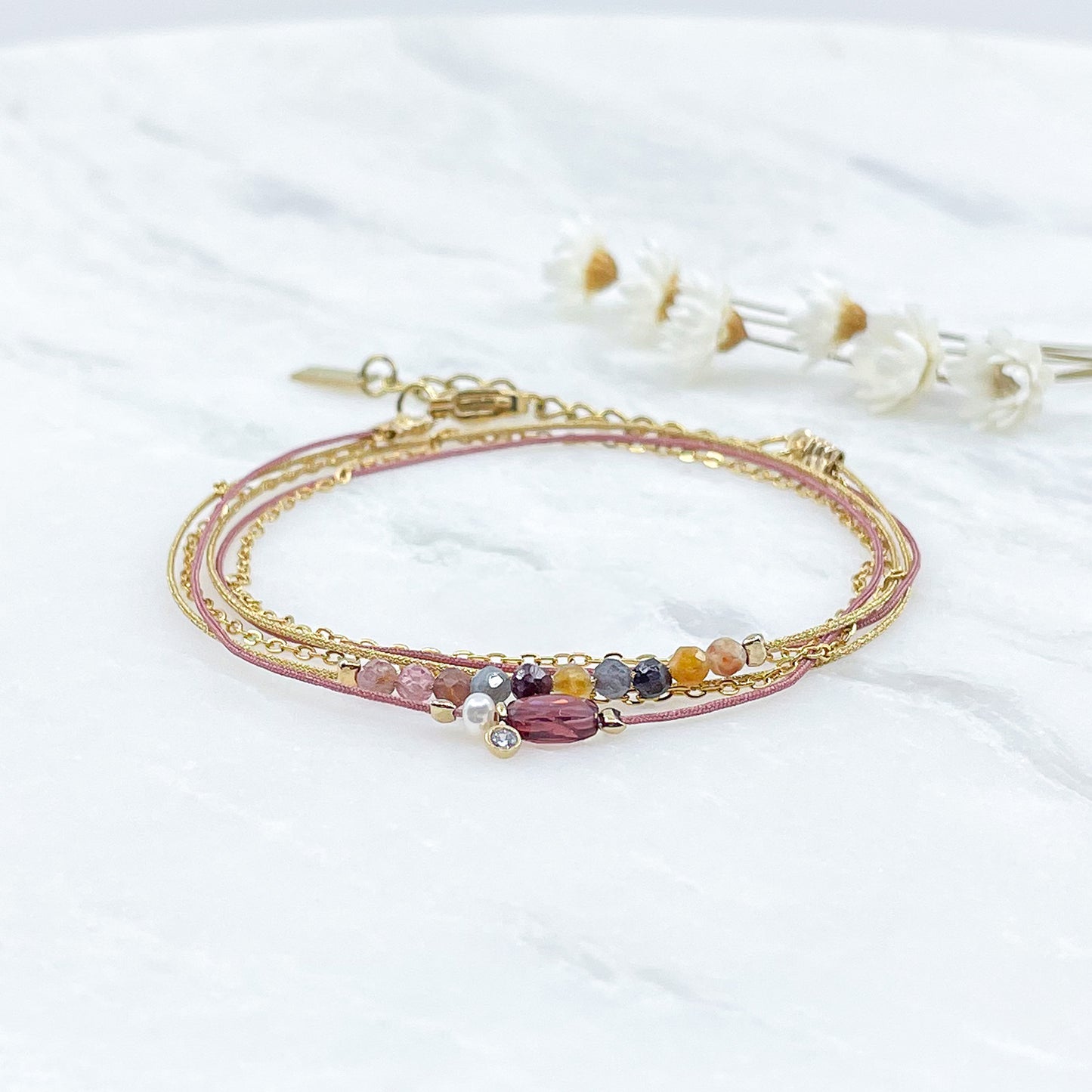 Bracelet composé de 3 liens cordons et chaîne s'enroulant en deux tours sur le poignet. Il met en valeur les perles de pierre naturelle de Tourmaline ainsi qu'un Grenat, une Perle de Culture et un petit pendentif serti d'un cristal. Pierres et perles sont montées sur les différents liens.