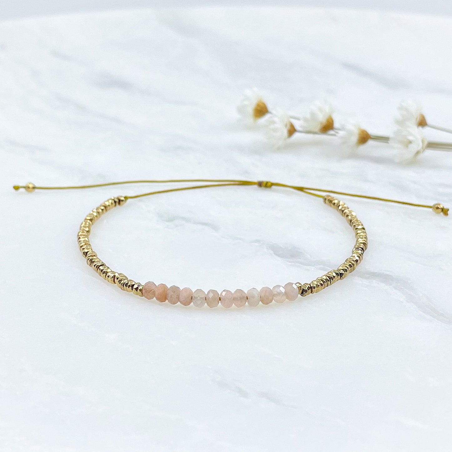 Bracelet ajustable en pierres fines naturelles Pierre de Soleil aux nuances rosées et perles d'hématites dorées.