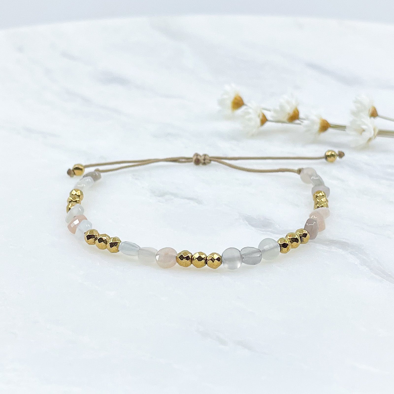 Bracelet ajustable en pierres fines naturelles Pierre de Soleil aux nuances blanches et rosées et perles d'hématites dorées.