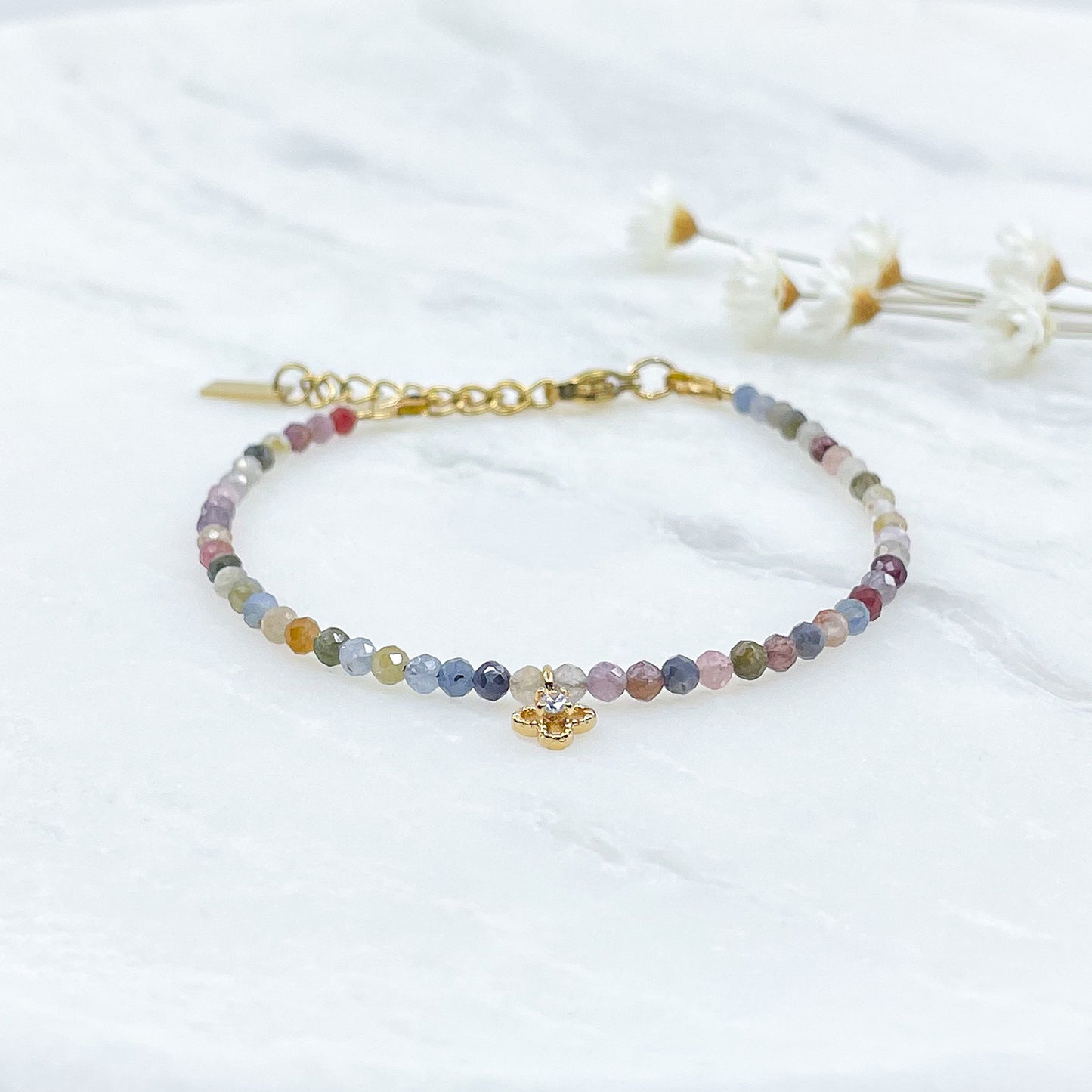 Bracelet pierres naturelles perles de tourmaline multicolores. En son centre un petit pendentif trèfle doré serti d'un cristal.