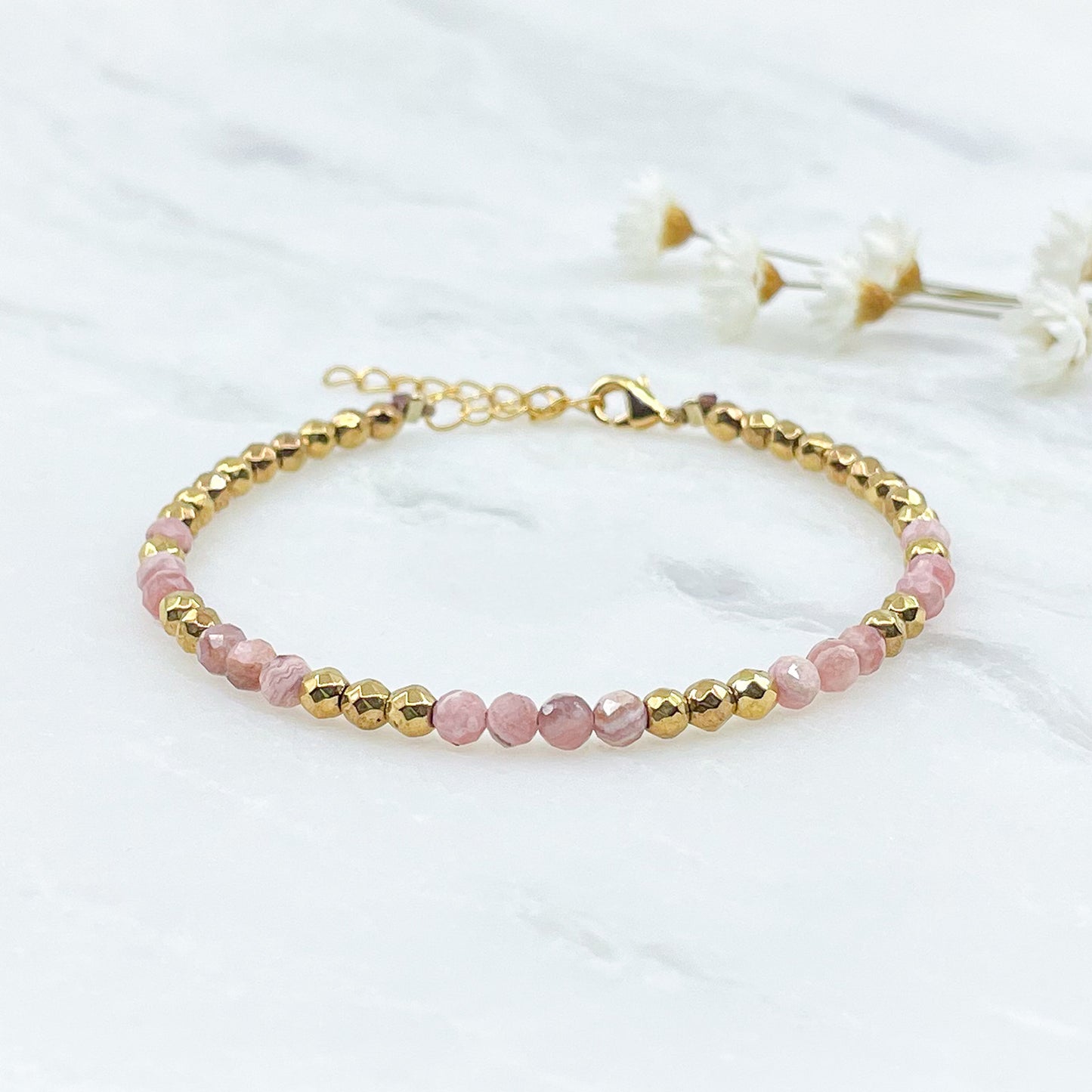 Rivière en pierres fines naturelles en perles facettées rose de rhodochrosite alternant avec des perles d'hématite dorée.