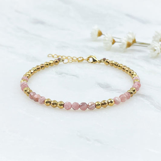 Rivière en pierres fines naturelles en perles facettées rose de rhodochrosite alternant avec des perles d'hématite dorée.