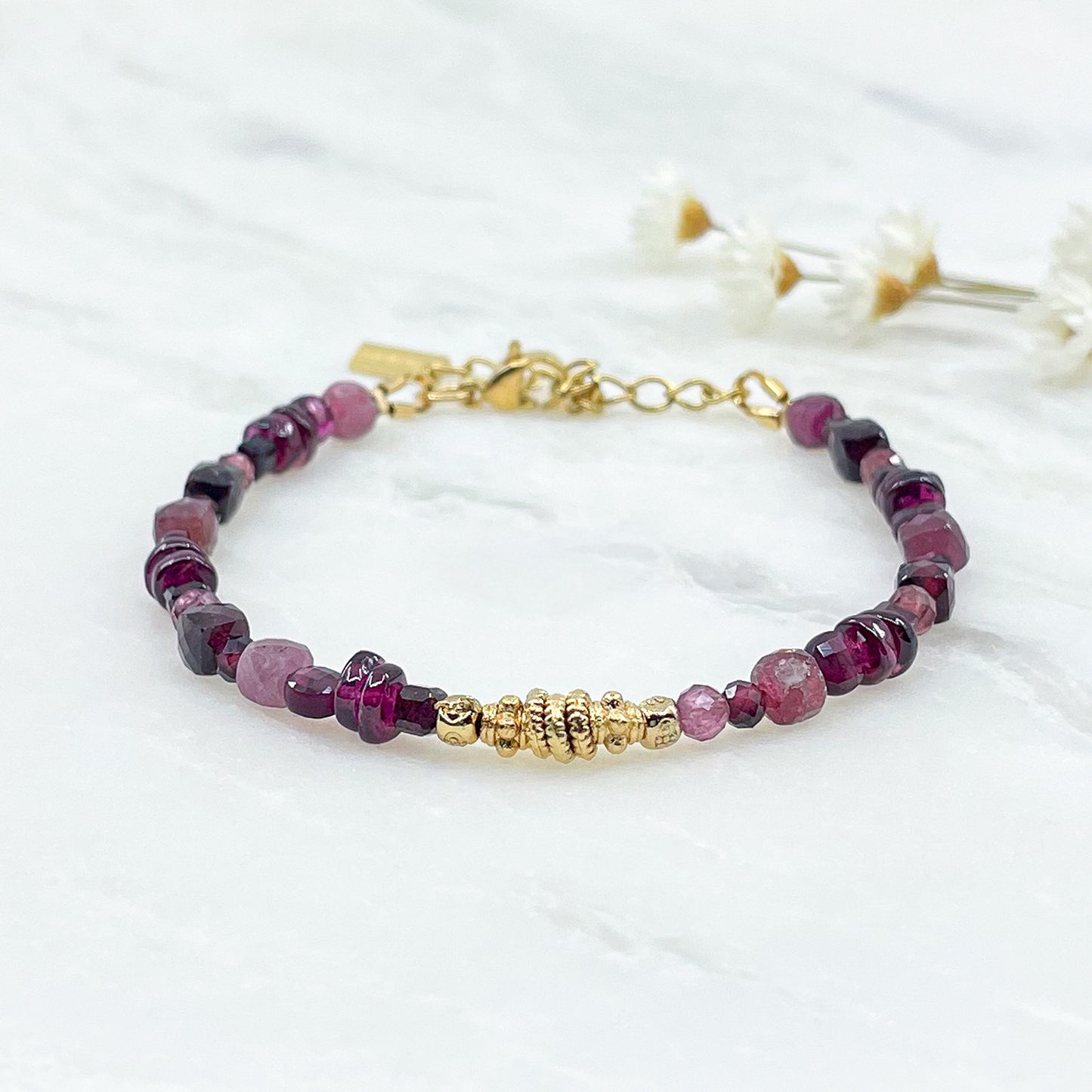 Bracelet pierres naturelles Tourmaline et Grenat dans une déclinaison de teintes bordeaux-rose profond. Perles dorées multiformes au centre du bracelet.