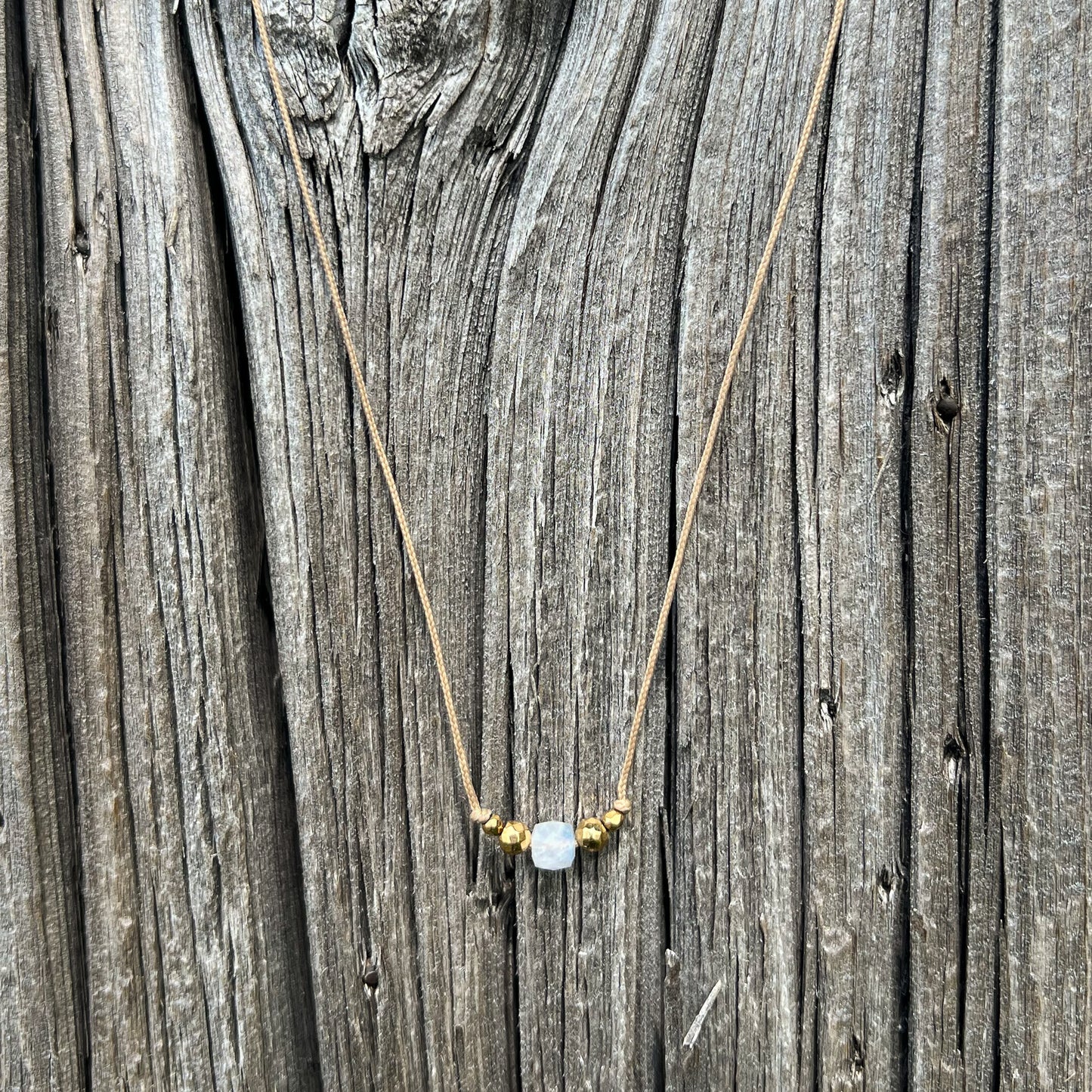 Collier cordon taille ajustable mettant en valeur une perle carrée facettée de pierre fine naturelle de Quartz Blanc entourée d'Hématite dorée.
