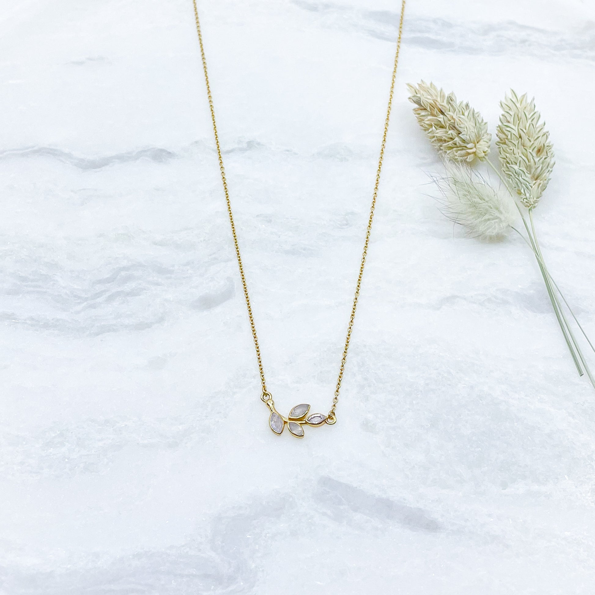 Collier plaqué or avec chaîne ajustable sur 3 niveaux de longueur différentes de 37 à 45 cm. Il met en valeur une brindille de feuillage réalisée en pierres fines naturelles de Pierre de Lune blanche au beaux reflets.