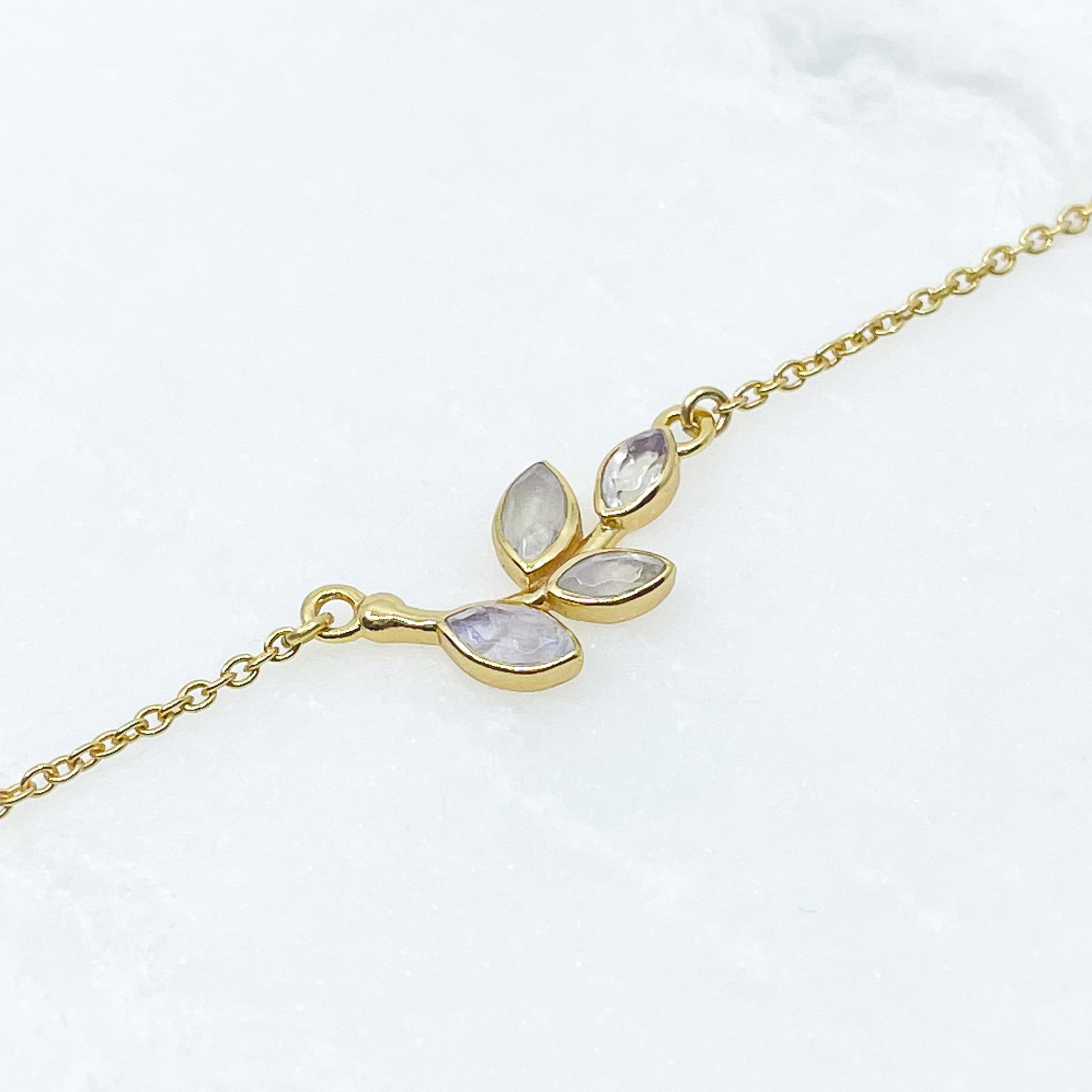 Collier plaqué or avec chaîne ajustable sur 3 niveaux de longueur différentes de 37 à 45 cm. Il met en valeur une brindille de feuillage réalisée en pierres fines naturelles de Pierre de Lune blanche au beaux reflets.