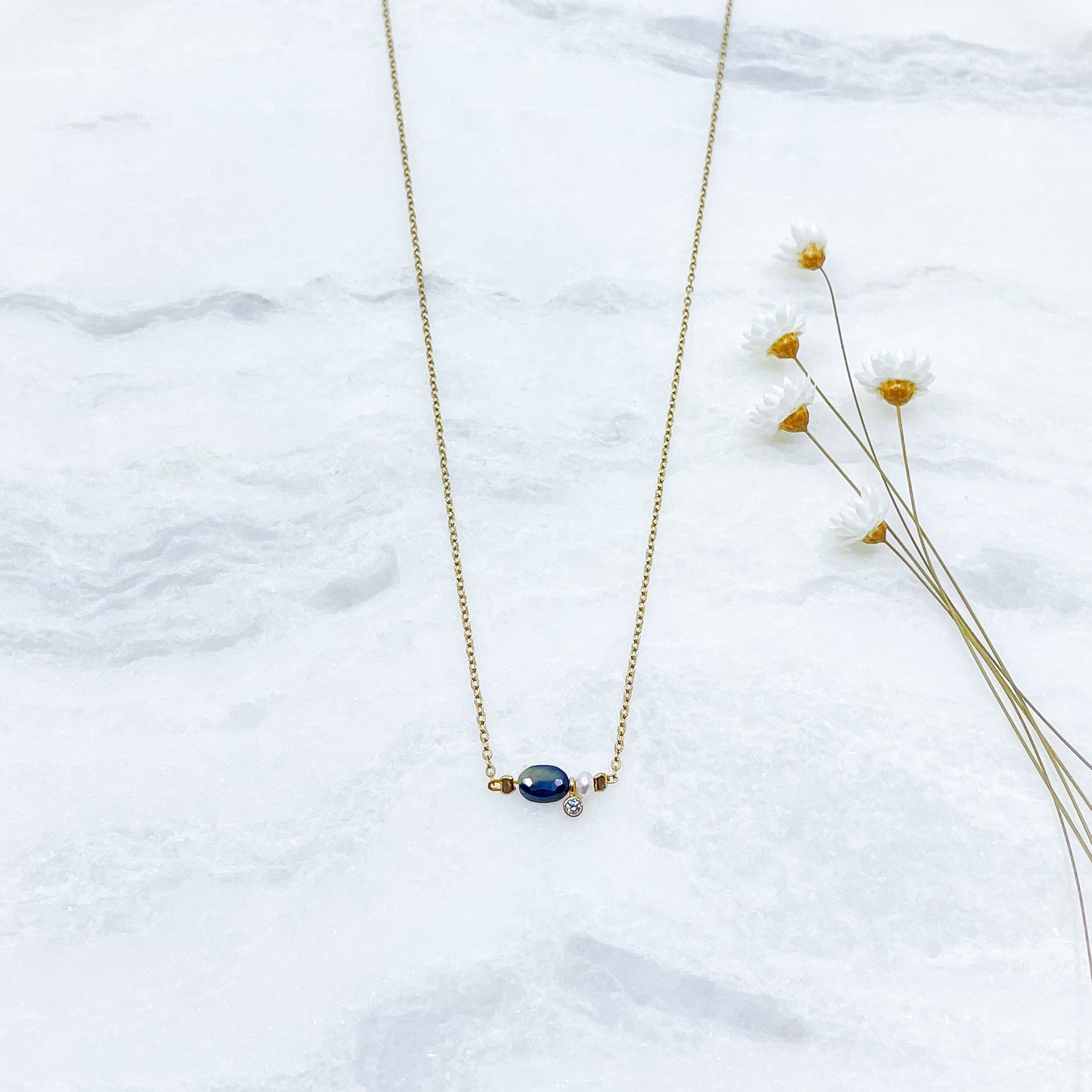 Collier en pierre fine naturelle Saphir Bleu orné d'une perle de culture et d'un petit pendentif cristal éclatant. Monté sur chaîne dorée en acier inoxydable.