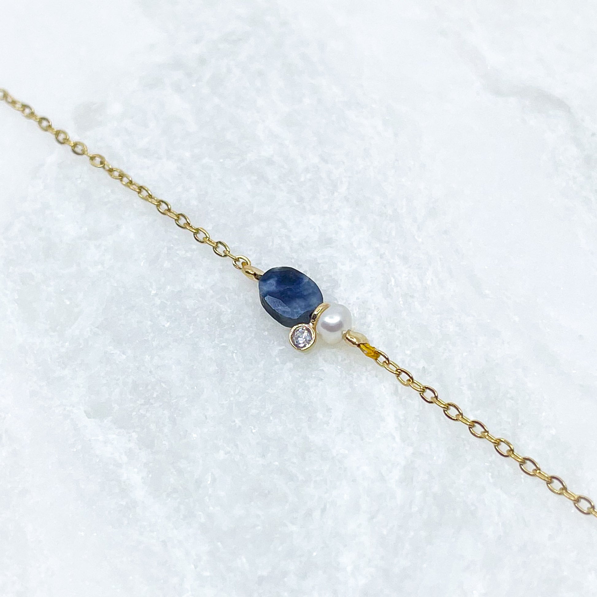 Collier en pierre fine naturelle Saphir Bleu orné d'une perle de culture et d'un petit pendentif cristal éclatant. Monté sur chaîne dorée en acier inoxydable.