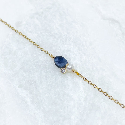 Collier en pierre fine naturelle Saphir Bleu orné d'une perle de culture et d'un petit pendentif cristal éclatant. Monté sur chaîne dorée en acier inoxydable.