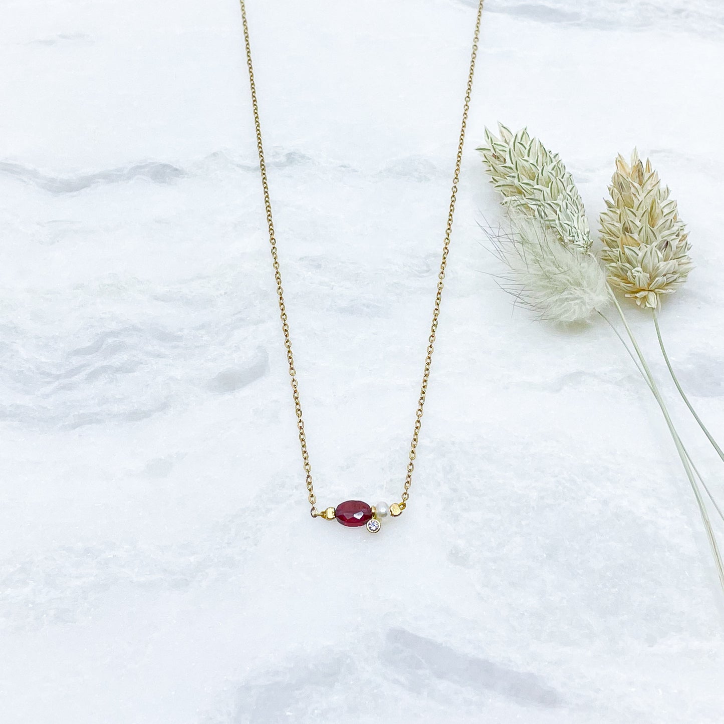 Collier en pierre fine naturelle Grenat orné d'une perle de culture et d'un petit pendentif cristal éclatant. Monté sur chaîne dorée en acier inoxydable.