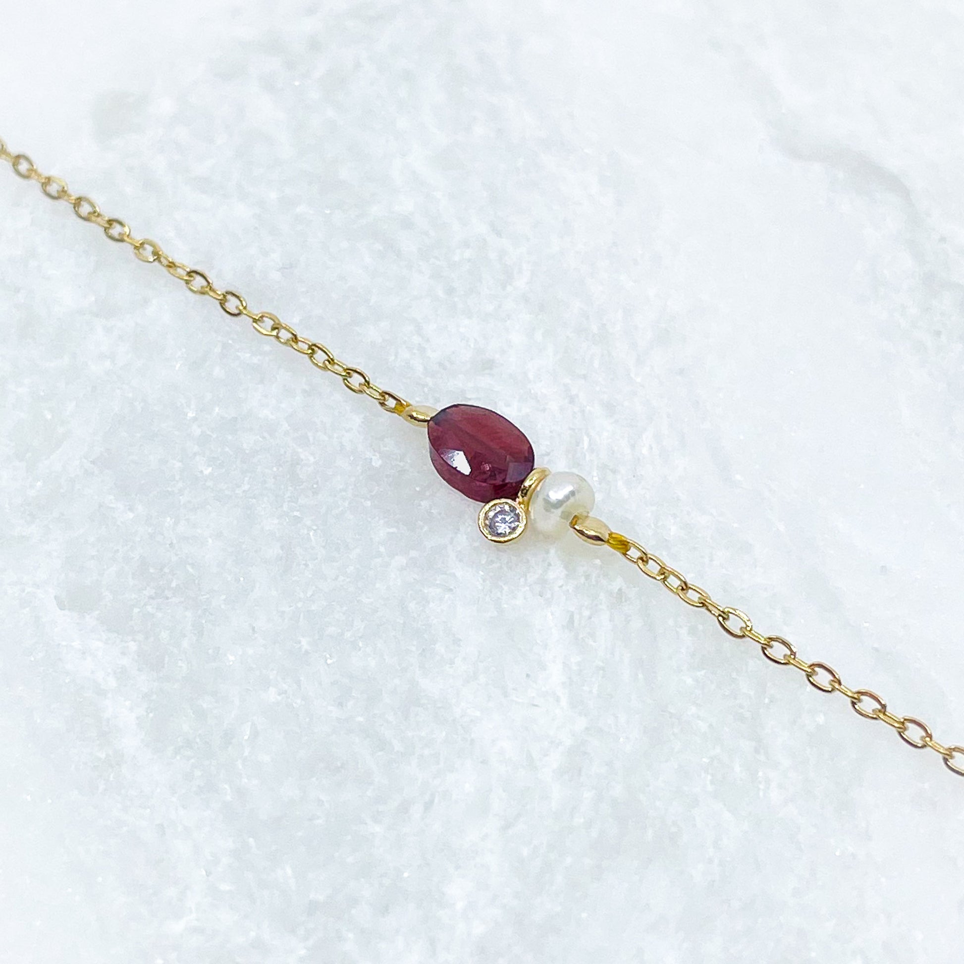 Collier en pierre fine naturelle Grenat orné d'une perle de culture et d'un petit pendentif cristal éclatant. Monté sur chaîne dorée en acier inoxydable.