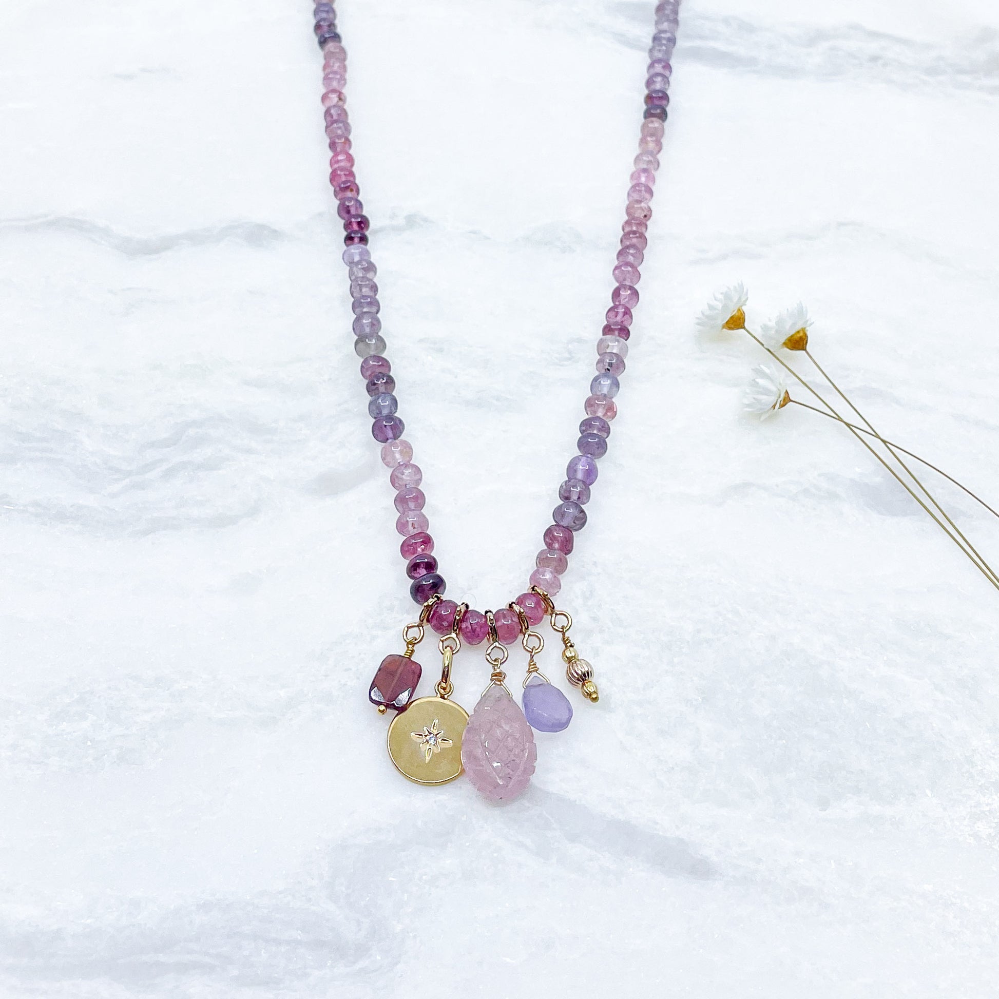 Collier long de 58 cm en pierres fines naturelles de spinelle dans des dégradés de rose à bleu gris. 5 charms : 3 pierres fines naturelles de teintes harmonieuses, une médaille ronde et un pendentif en petites perles plaqué or. Chaîne de réglage de 4 cm et fermoir plaqué or 18 carats